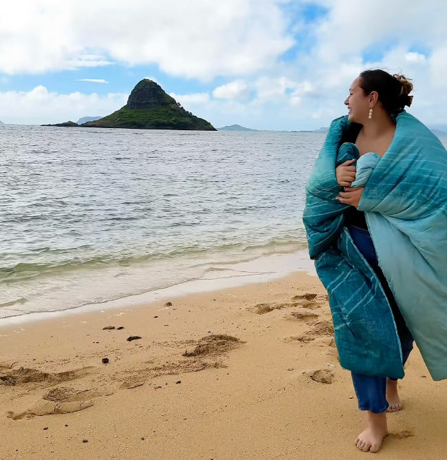 woman standing near ocean wrapped in a teal blanket