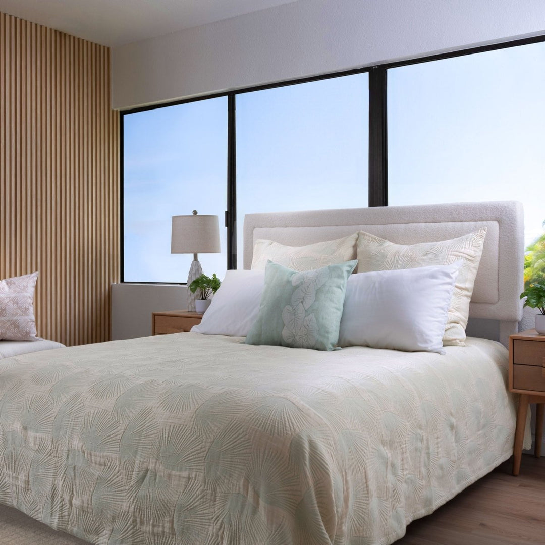 Loulu green coverlet on bed with fan palm pattern, styled with pillows and tropical greenery in a lush home setting.