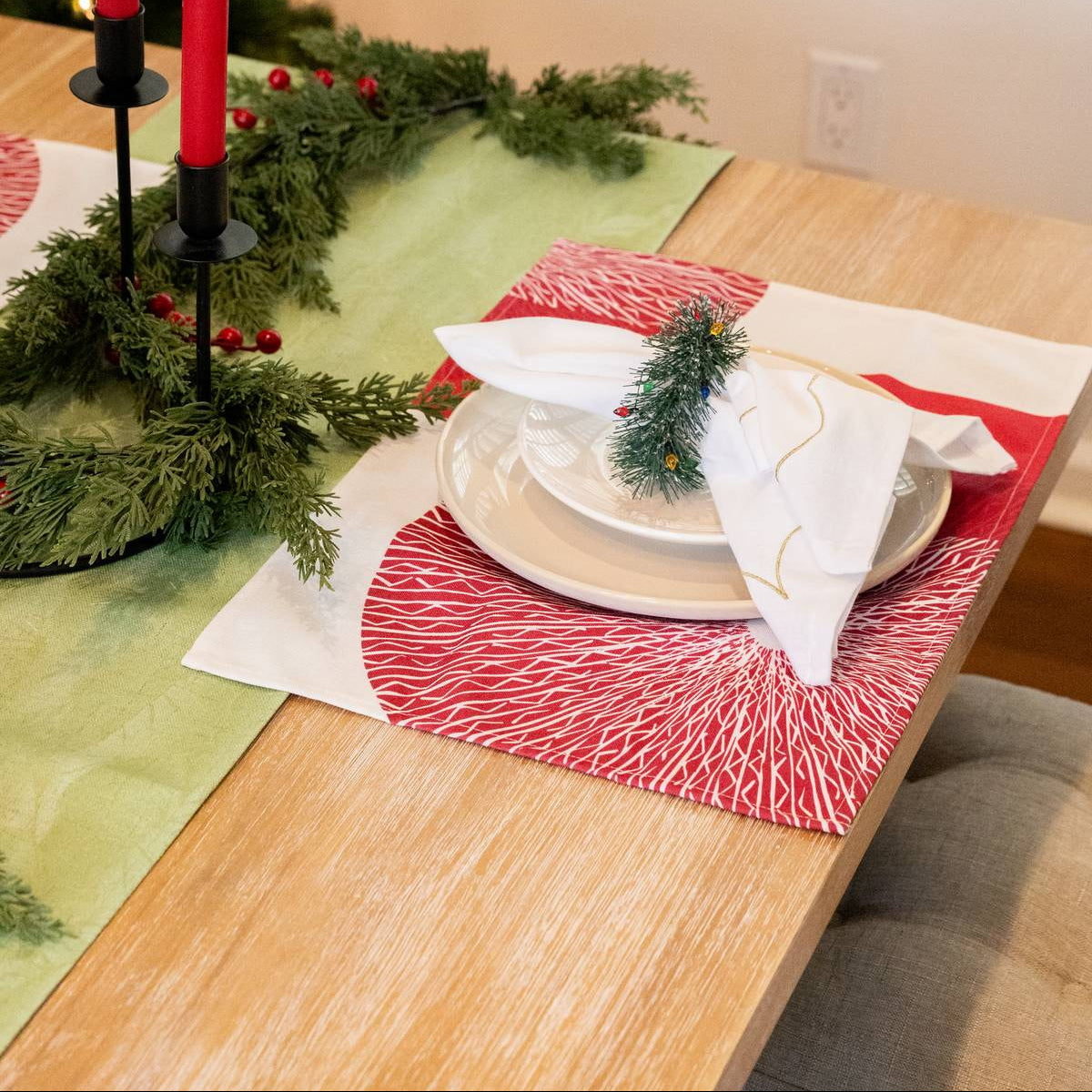 Christmas table setting with red candles, greenery, and white napkins.