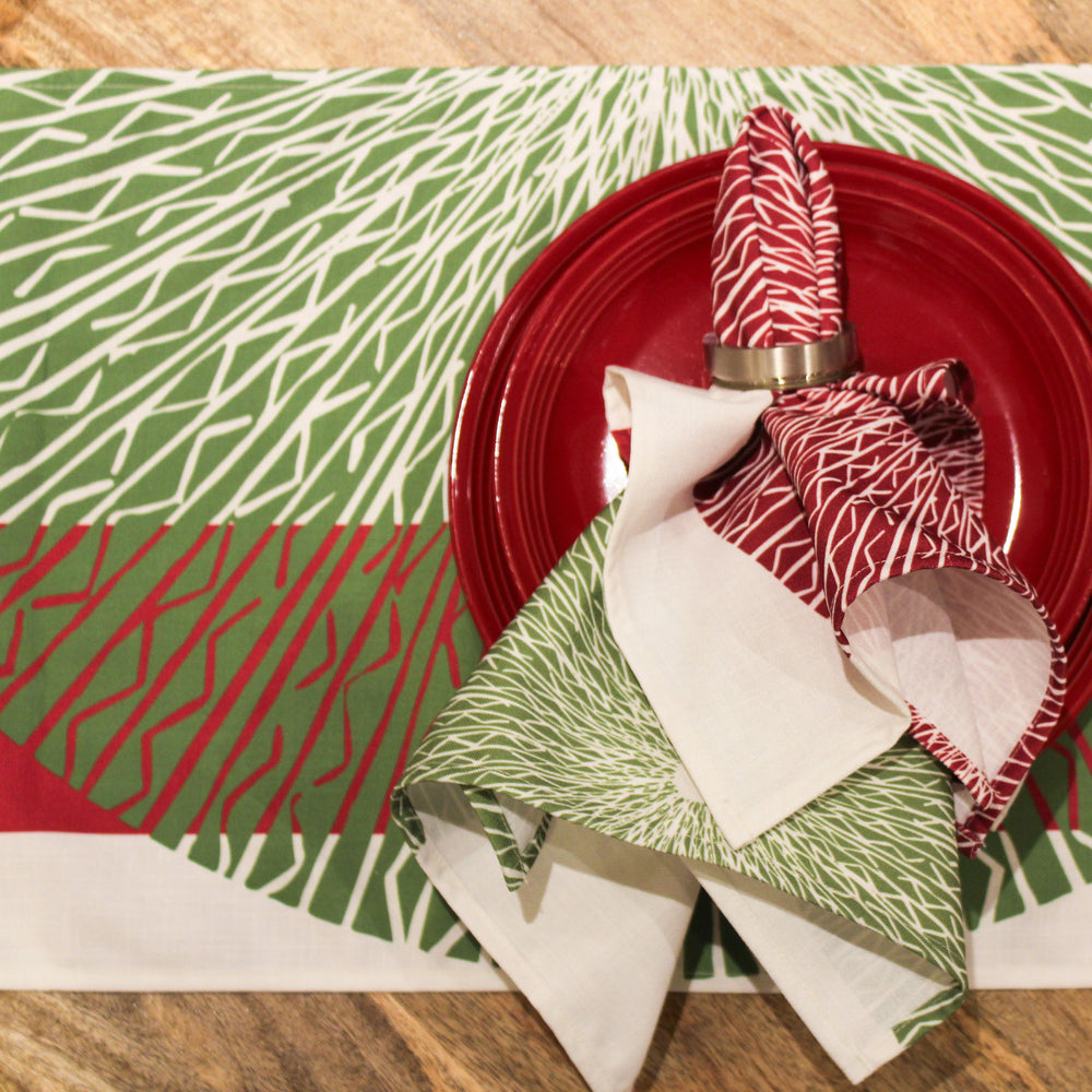 Red & Green Niho Medallion Table Runner beneath red plate with Red & Green Niho Medallion Dining Napkin encircled by brass napkin ring.