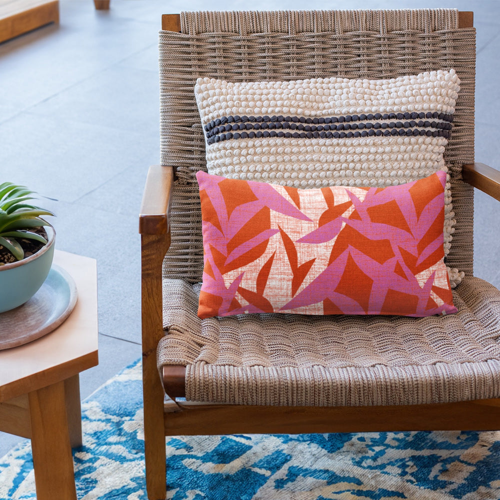 Hibiscus Lele Lumbar Pillowcase placed against knotted square pillow on a woven chair.  Wooden side table with succulent.  