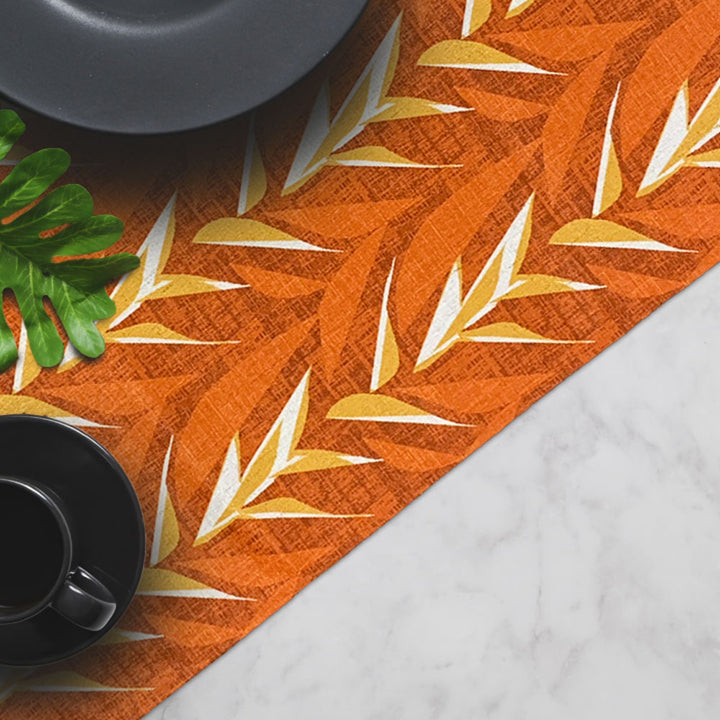 Premium Ulu Mau Orange and Gold Hawaiian Print Table Runner Set On a Table With a Black Plate and Cup and Saucer