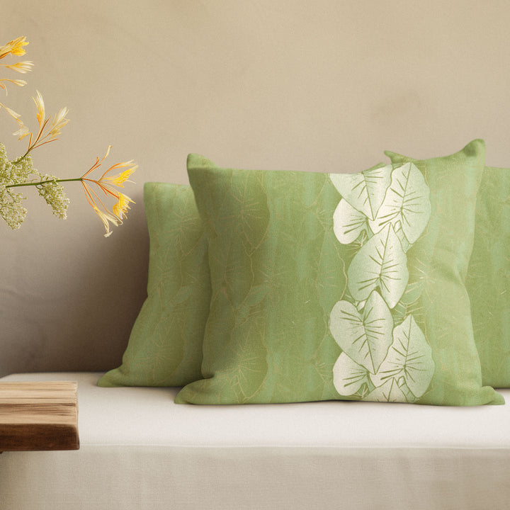 Green pillows with kalo leaf pattern on a beige sofa against a beige wall.