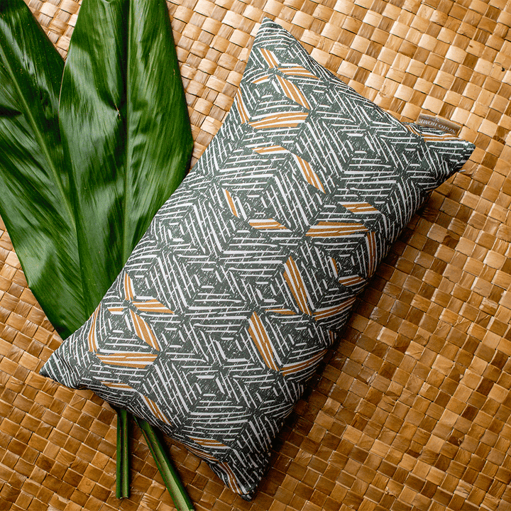 Stone & Bark 'Akahi Lumbar Pillowcase resting on some ti leaves on a woven lauhala mat
