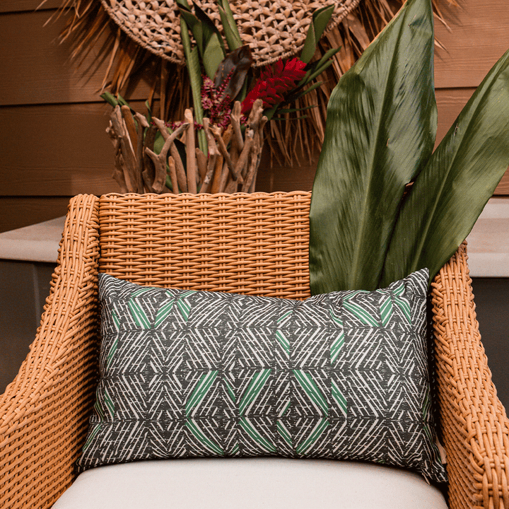 Forest & Stone 'Akahi Lumbar Pillowcase in a rattan chair with leafy green accents and Hawaiian artwork in background