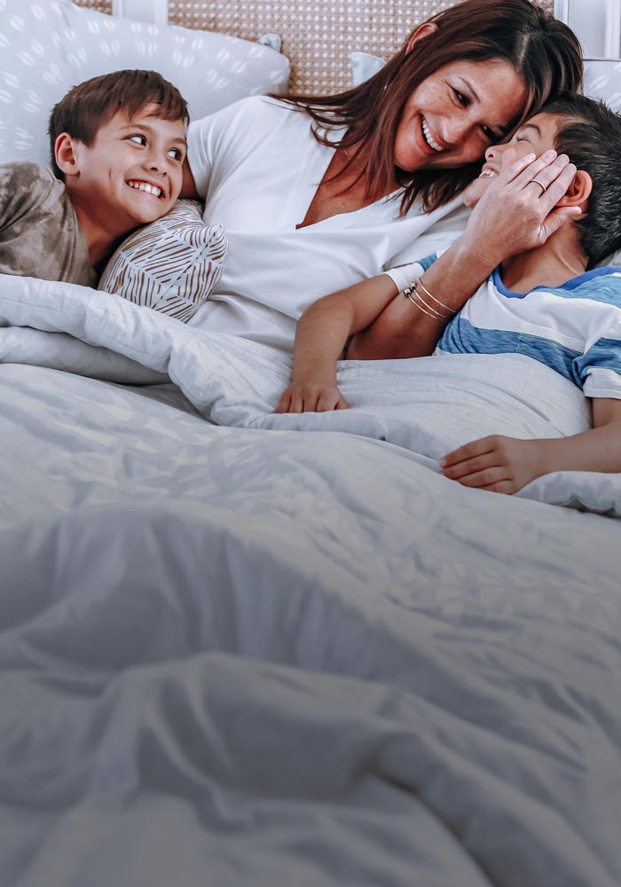 Mother and Two Sons Smiling and Laughing on a White Bed With Coastal Home Decor Interior Design