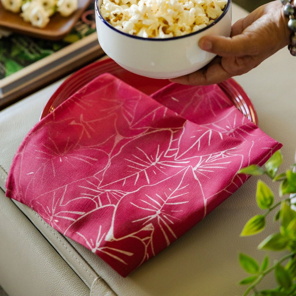 Hand holding a bowl of popcorn over a pink floral-patterned Dining napkin on a couch.