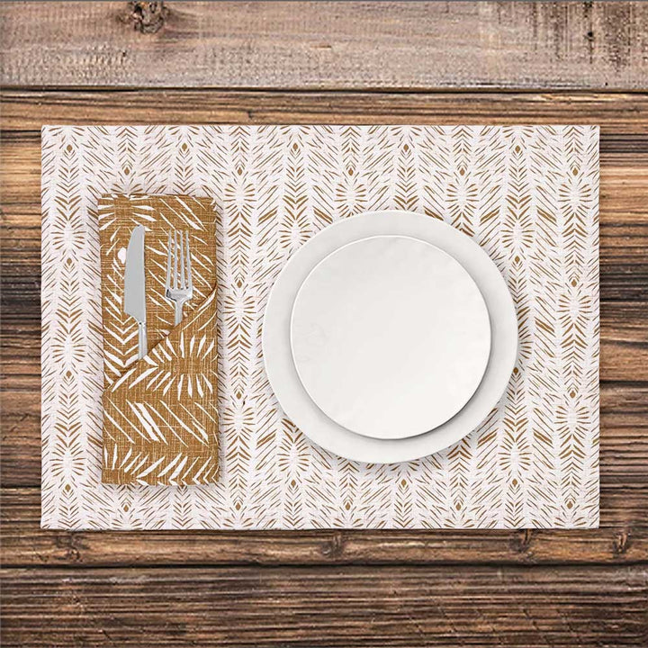A place setting showcasing the Hulu Dining Placemat and Hulu Napkin, both in Gold,  with a white plate and cutlery