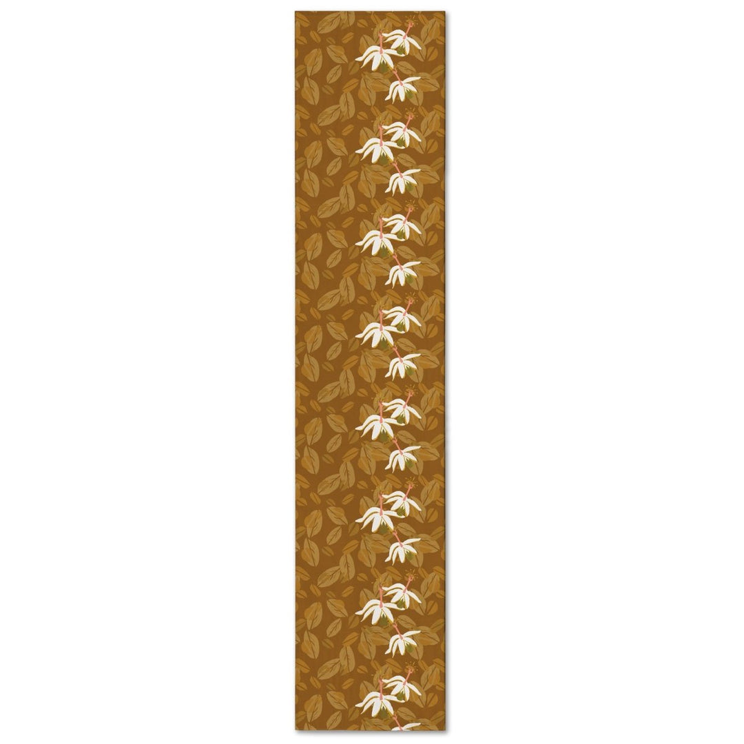 Caramel Kokiʻo Table Runner with cream blossoms down the center over tonal leaves, shown full length on a white background