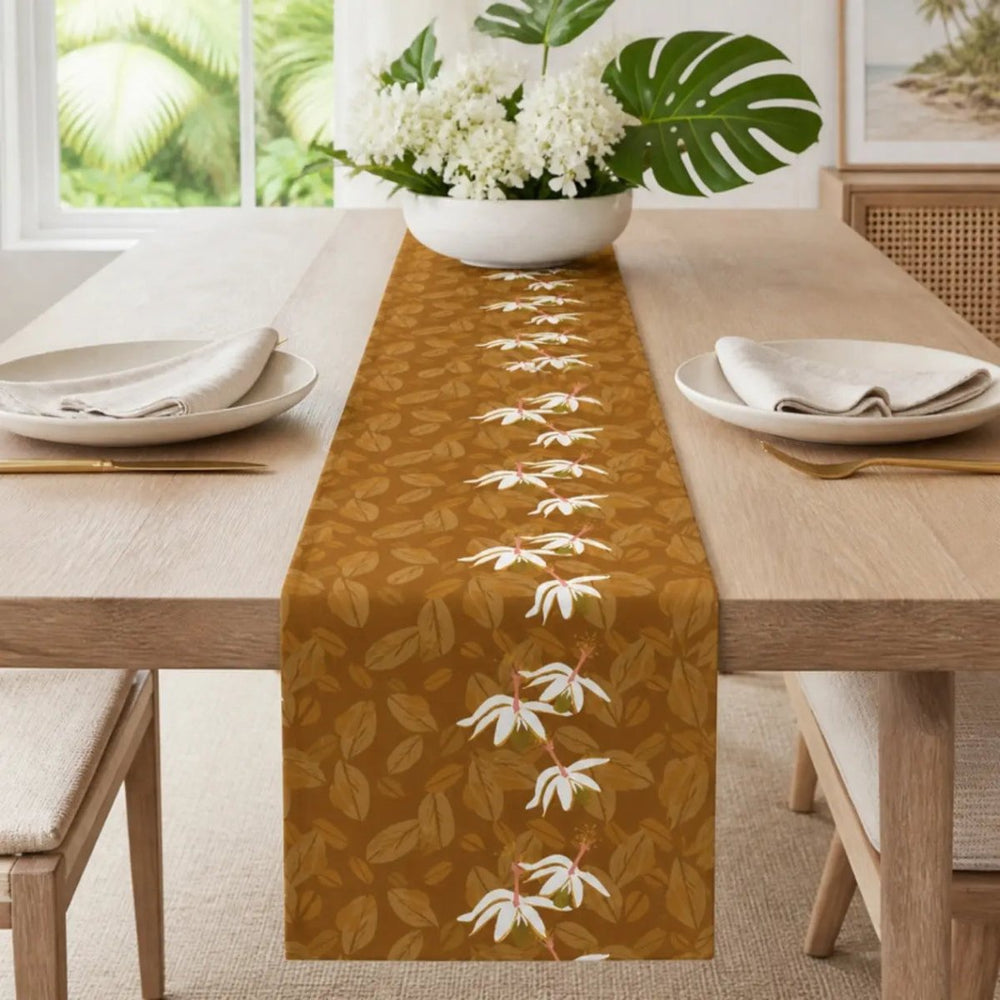 Caramel Kokiʻo Table Runner styled down a white-oak dining table with cream plates, linen napkins, brass flatware and a bowl of white flowers and monstera