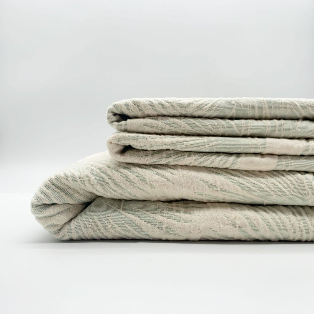 Loulu green matelasse coverlet folded featuring fan palm pattern.
