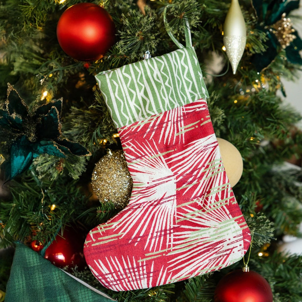 Red and green patterned Christmas stocking hanging on a decorated tree.