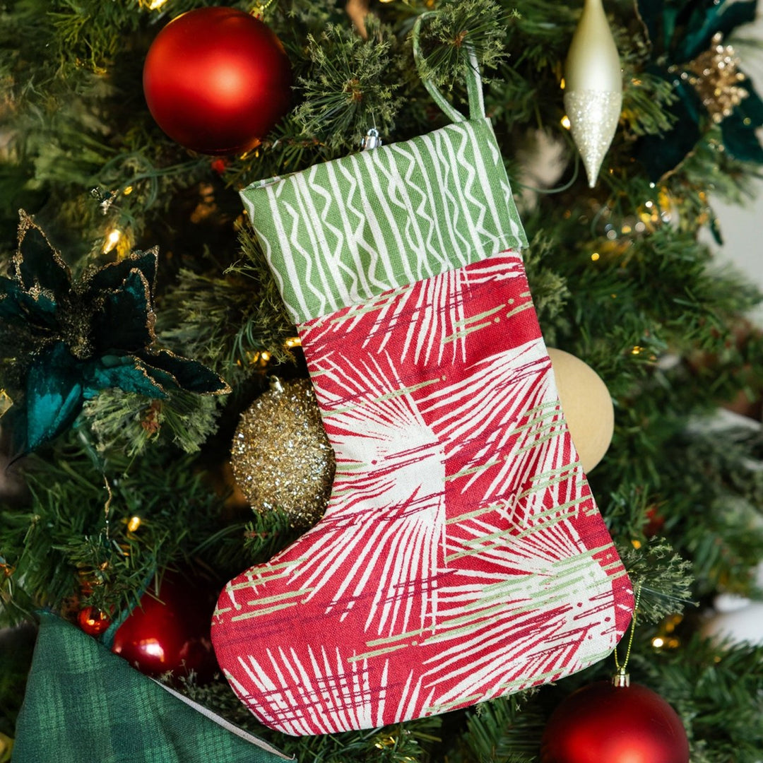 Red and green patterned Christmas stocking hanging on a decorated tree.