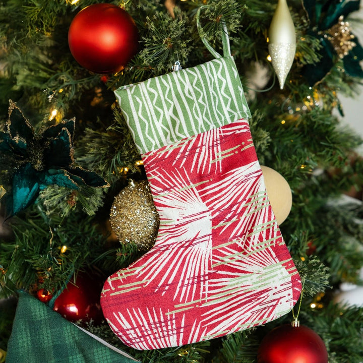 Red and green patterned Christmas stocking hanging on a decorated tree.