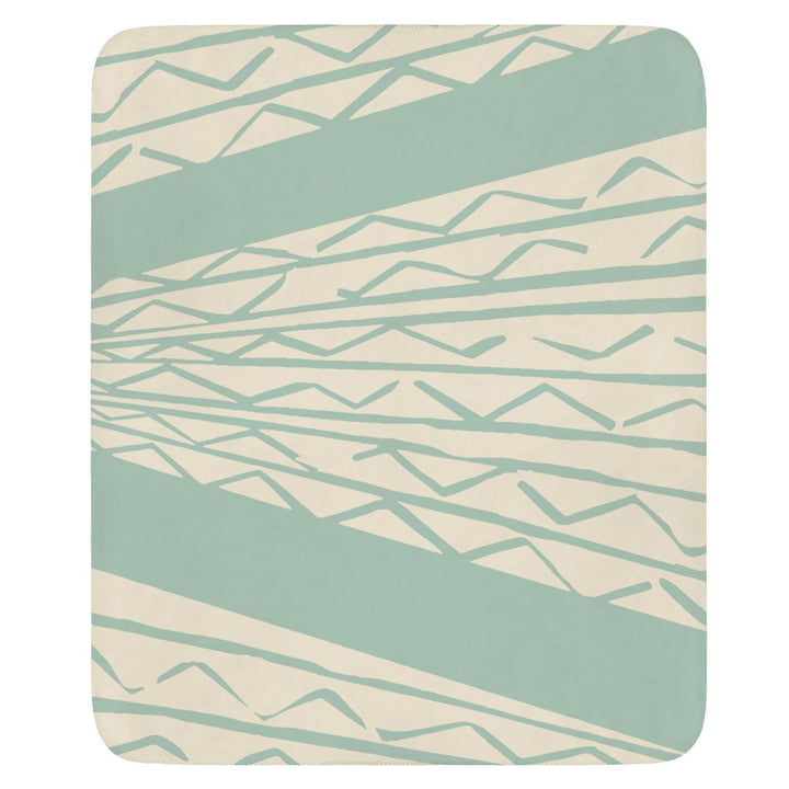 A cozy throw blanket with a geometric niho kila pattern, featuring sharp triangular motifs in shades of blue and white, draped over a chair in a living room setting.