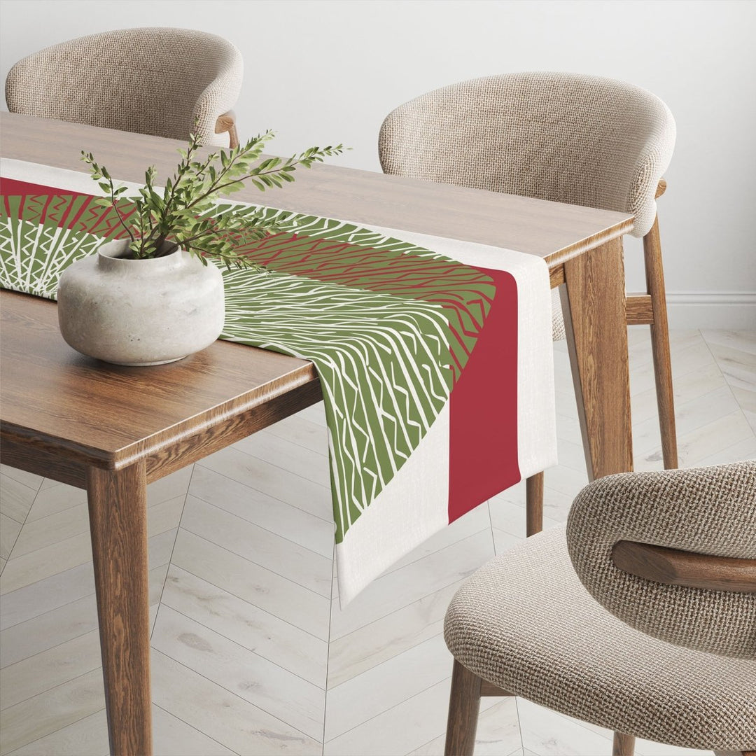 Red & Green Niho Medallion Table Runner draped across wooden table, accompanied by a potted plant and several mid-century modern chairs.