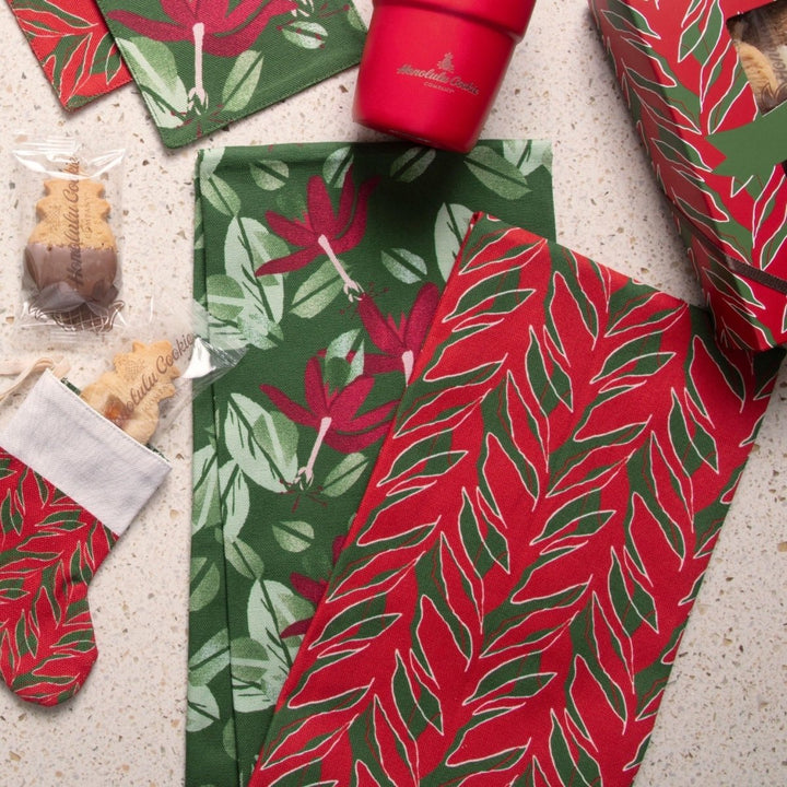 Kī and Kokiʻo ʻUlaʻula tea towels styled with a mini stocking, shortbread and a red tumbler