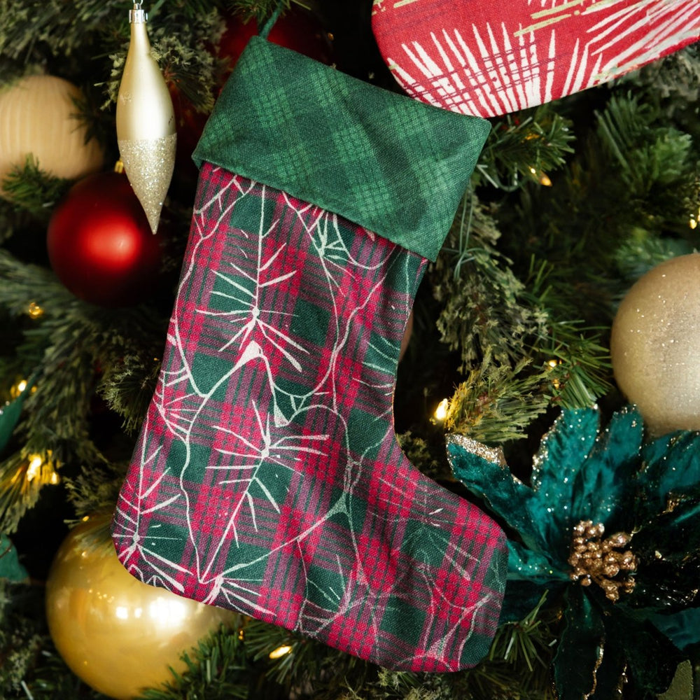 Plaid Christmas stocking hanging on a decorated tree with ornaments.