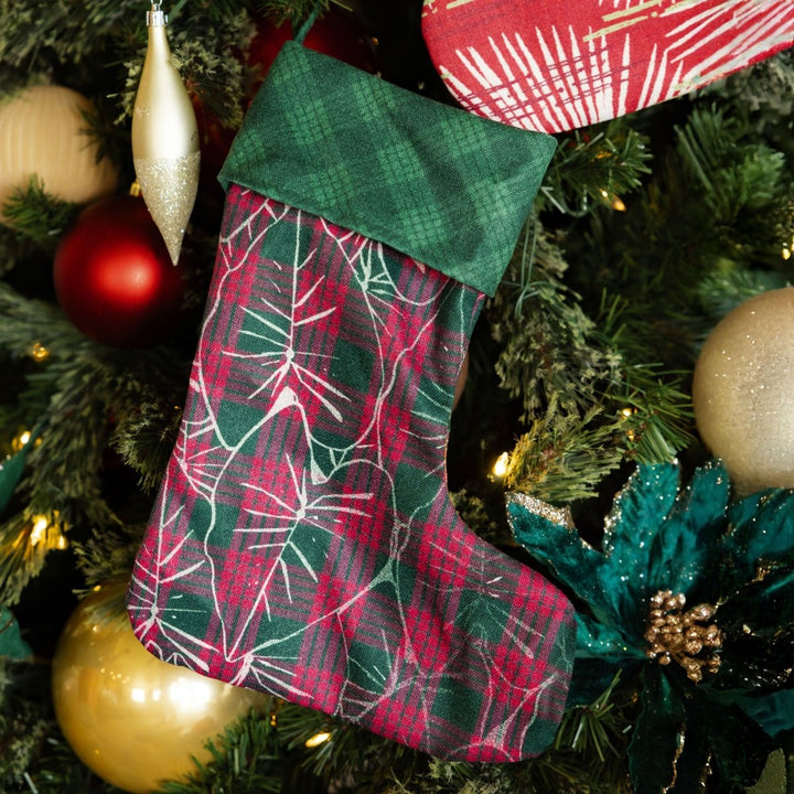 Plaid Christmas stocking hanging on a decorated tree with ornaments.