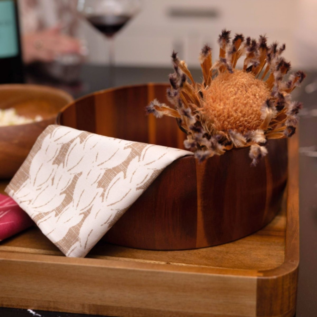 Wooden bowl with decorative flower and patterned tea towel on a wooden surface