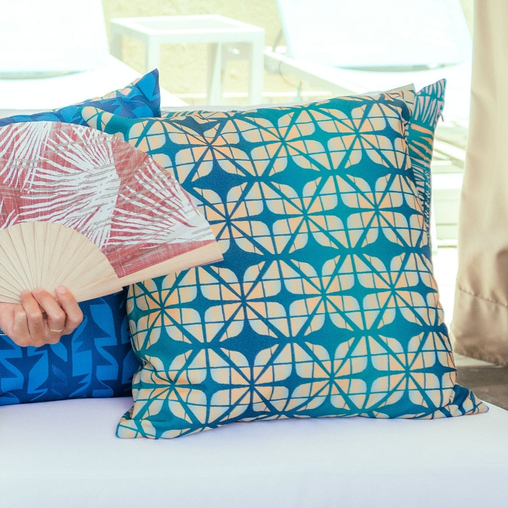 Decorative pillows with geometric patterns on a bed, held by a person with a fan.