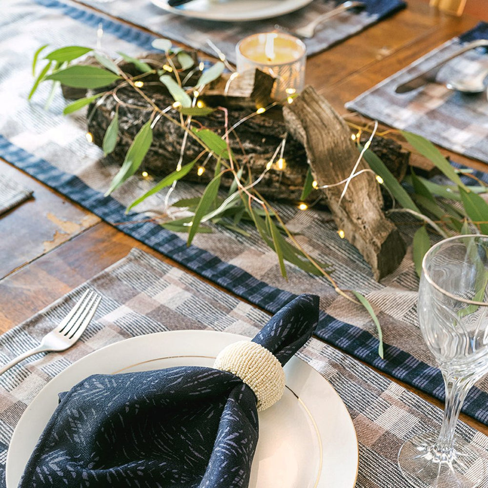 Pūlehu Premium Papamū Table Runner under natural centerpiece, along with place settings of Papamū Dining Placemats, Black Batik napkins with flatware, plates and wine glasses.