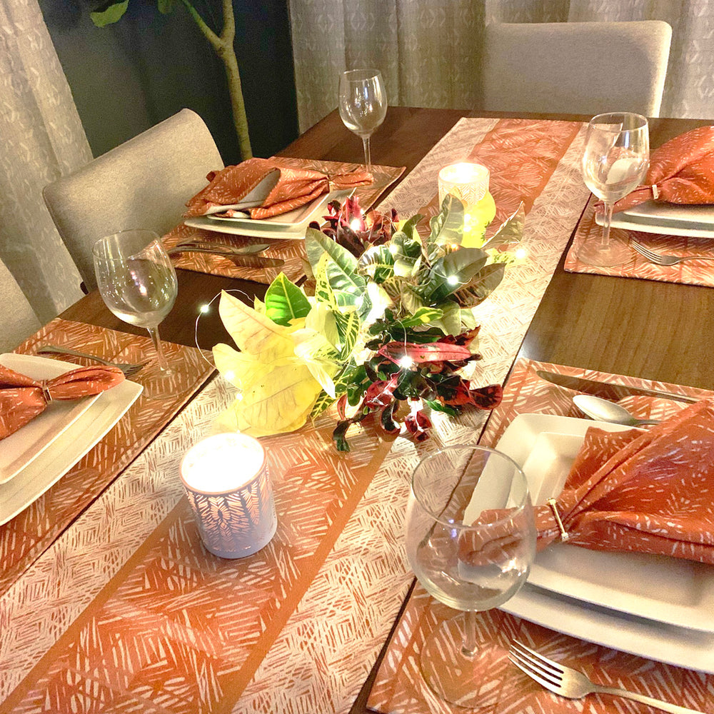 Pumpkin Premium Moena Table Runner on table with a candle and centerpiece, surrounded by four place settings of the Pumpkin Moena print and Batik napkin set.