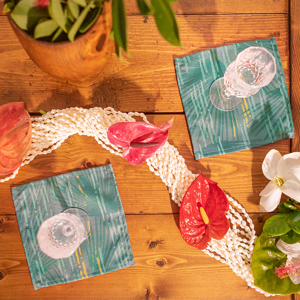 Blue Loulu Cocktail Napkin Set with crystal wine glasses and accented with anthuriums, hibiscus and Niʻihau shell lei. 