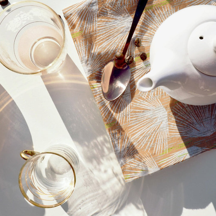 Teapot and spoon resting on Ivory and Orange Loulu Dining Napkin 