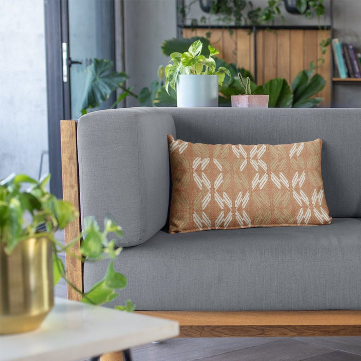 Sunset Peʻa Lumbar Pillowcase on a grey sofa with a variety of plants in the background