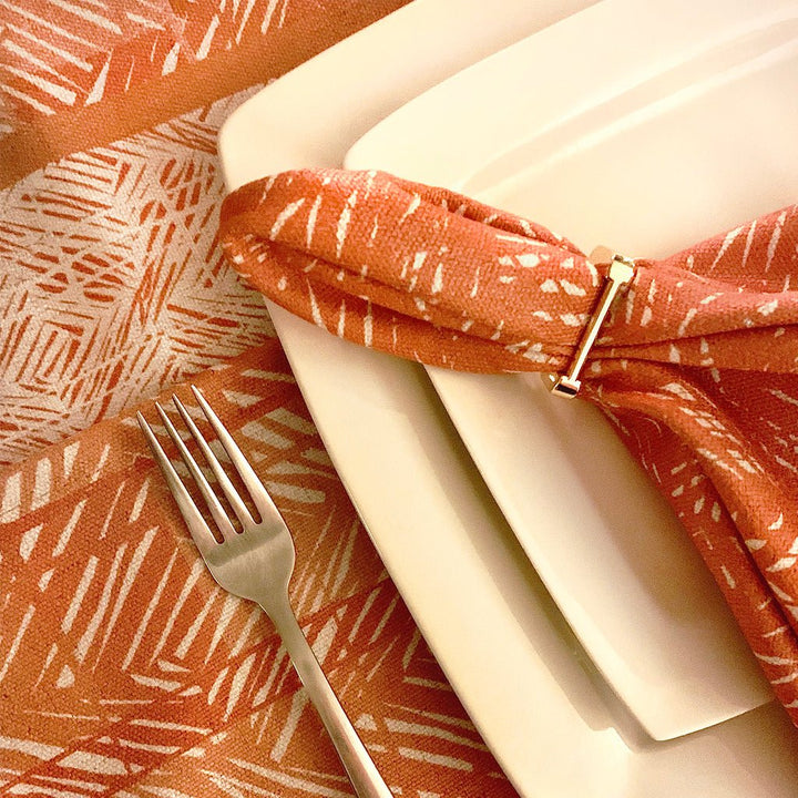 Pumpkin Premium Batik Dining Napkin with silver accent napkin ring on double ceramic plates and silverware.  Moena placemat in background