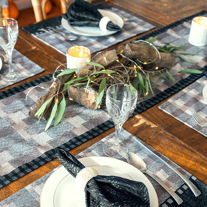 Pūlehu Premium Papamū Table Runner under natural centerpiece, along with place settings of Papamū Dining Placemats, Black Batik napkins with flatware, plates and wine glasses.