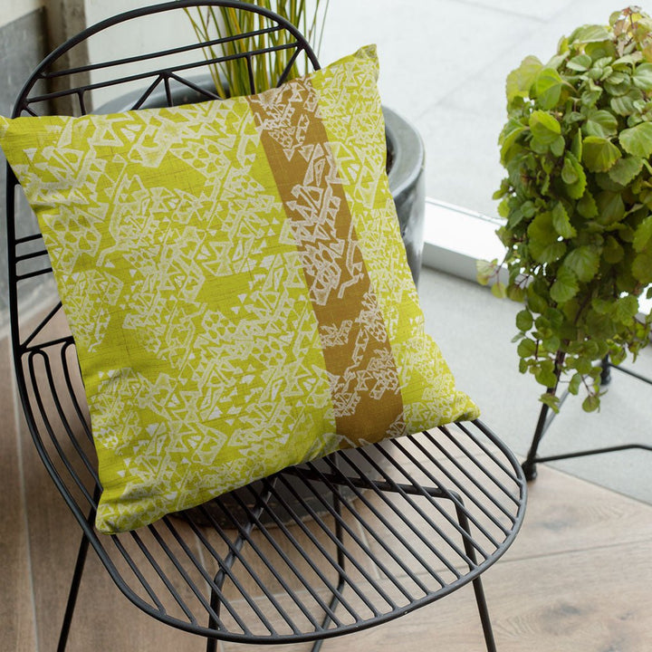 Pūpū Kuahiwi Square Pillowcase atop a metal chair surrounded by plants in a cozy space