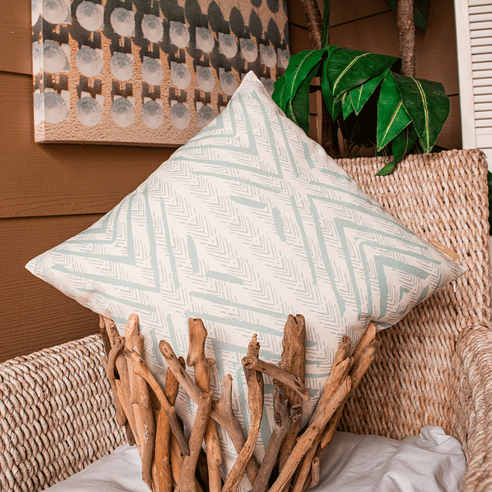 Light Blue and Beige Tiki Square Pillowcase in a woven branch basket, sitting atop a rattan chair with a tree in back